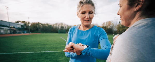 Female runner in blue t shirt looking at sports watch stood next to running track before workout on a sunny day